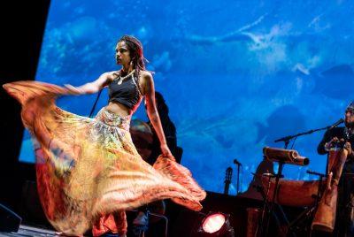  Indigenous woman wears a long flowing orange skirt, which is blurred as she twirls it on stage.